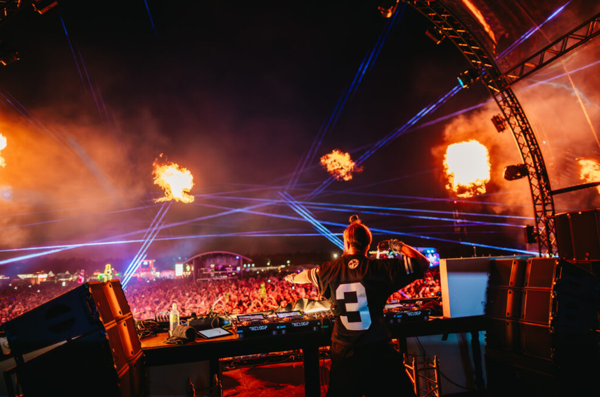 DJ grający na scenie podczas Sunrise Festival 2025, z efektem świetlnym i ogniami w tle.