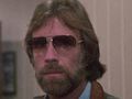Mężczyzna z brodą i okularami przeciwsłonecznymi, w tle ściana w odcieniu beżu.