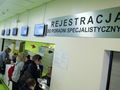 Rejestracja w poradni specjalistycznej, widoczni pacjenci przy oknie rejestracyjnym.