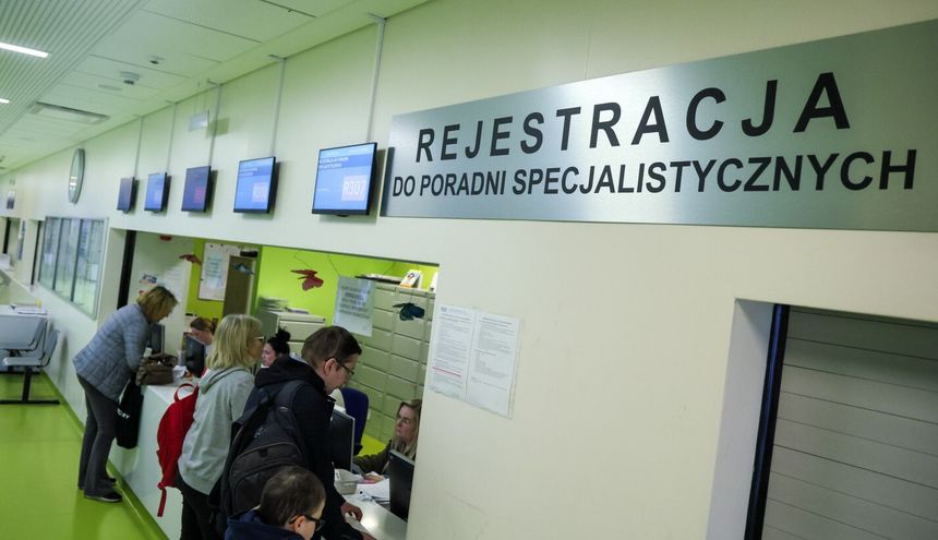 Rejestracja w poradni specjalistycznej, widoczni pacjenci przy oknie rejestracyjnym.