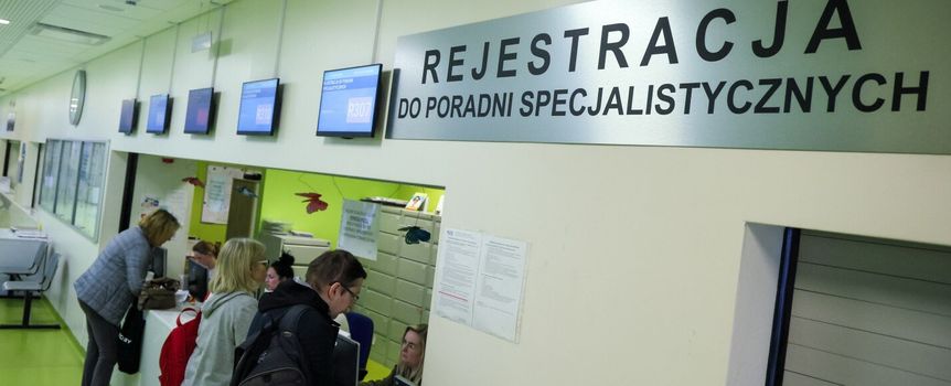 Rejestracja w poradni specjalistycznej, widoczni pacjenci przy oknie rejestracyjnym.
