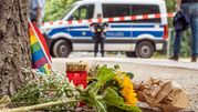 Na zdjęciu leżą kwiaty i znicz przy policyjnej furgonetce, w tle widać ludzi i tęczową flagę.