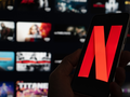 Na zdjęciu widoczny telefon z logo Netflix na tle rozmazanego interfejsu aplikacji