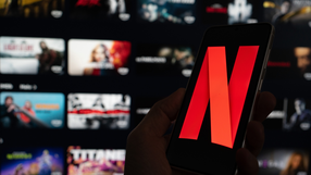 Na zdjęciu widoczny telefon z logo Netflix na tle rozmazanego interfejsu aplikacji