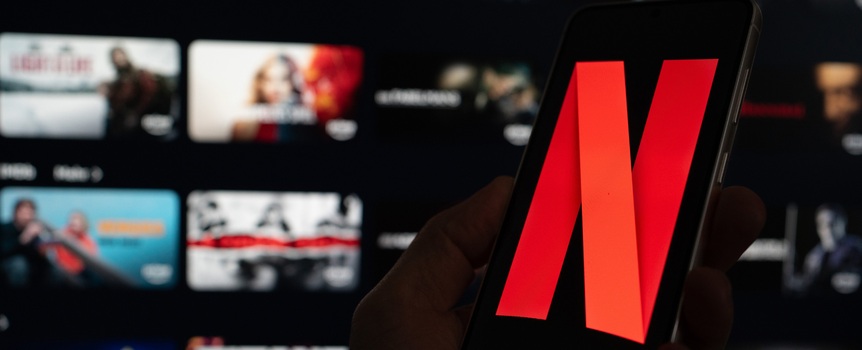 Na zdjęciu widoczny telefon z logo Netflix na tle rozmazanego interfejsu aplikacji