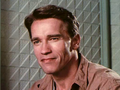 Arnold Schwarzenegger z krótkimi brązowymi włosami, uśmiecha się w jasnym otoczeniu.