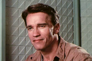 Arnold Schwarzenegger z krótkimi brązowymi włosami, uśmiecha się w jasnym otoczeniu.