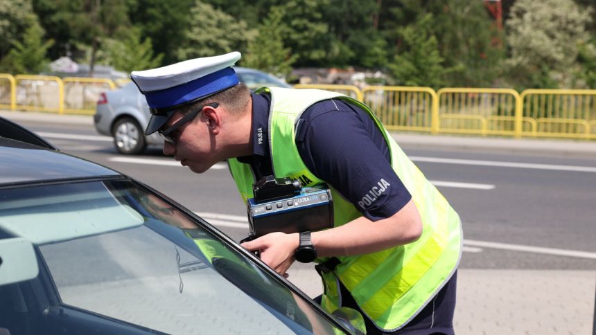 Policjant z urządzeniem pomiarowym sprawdza samochód na drodze w słoneczny dzień.