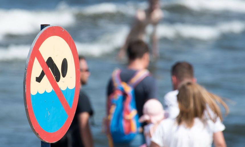 Zakaz pływania, w tle plaża z ludźmi i falami. Bez rozpoznawalnych polityków.
