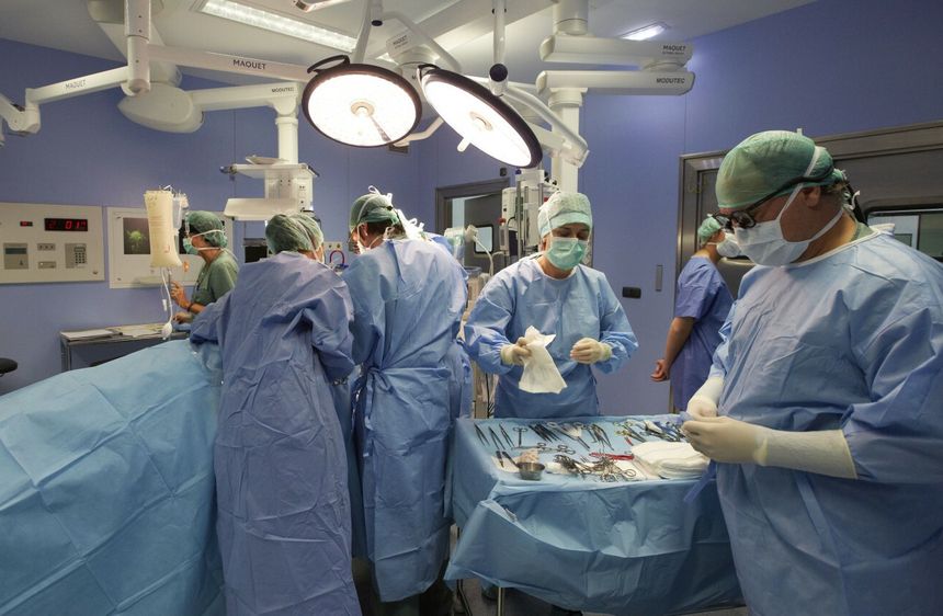Grupa chirurgów w niebieskich ubraniach operacyjnych, pracujących w sali operacyjnej.