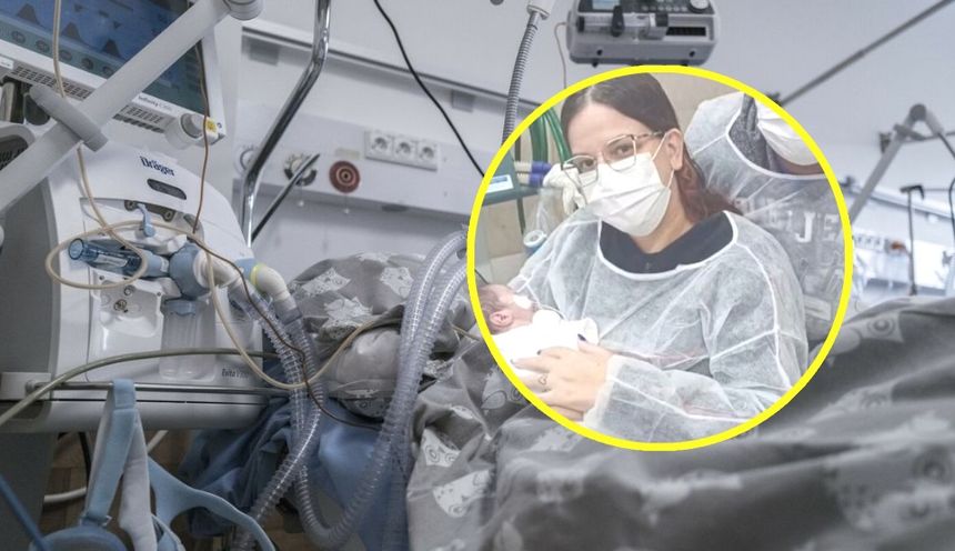 Kobieta w maskę trzyma noworodka w otoczeniu sprzętu medycznego w szpitalu.