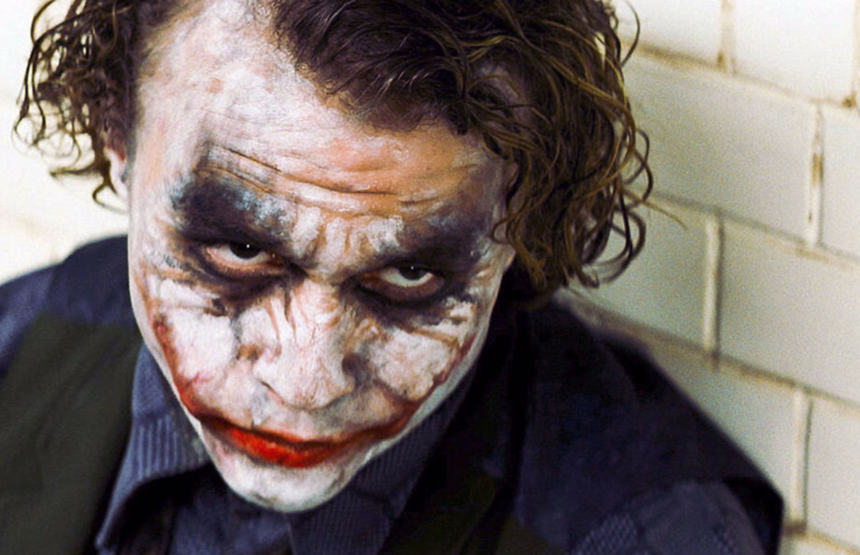 Na zdjęciu Joker z wyrazem twarzy sugerującym złośliwość, w zniszczonym makijażu.