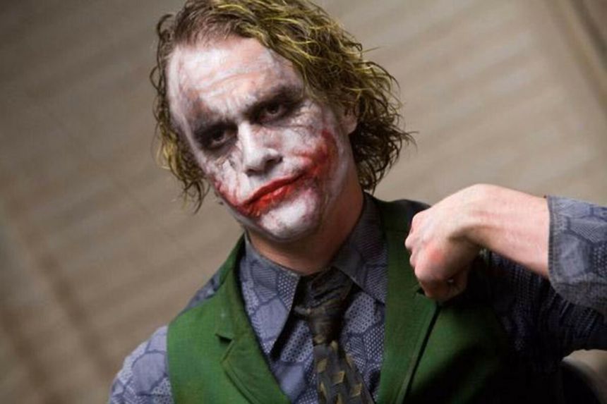 Mężczyzna w zielonej kamizelce z białą twarzą i czerwonym uśmiechem. To Joker z komiksów.