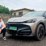 Mężczyzna z długimi włosami w okularach przeciwsłonecznych przy samochodzie marki CUPRA.