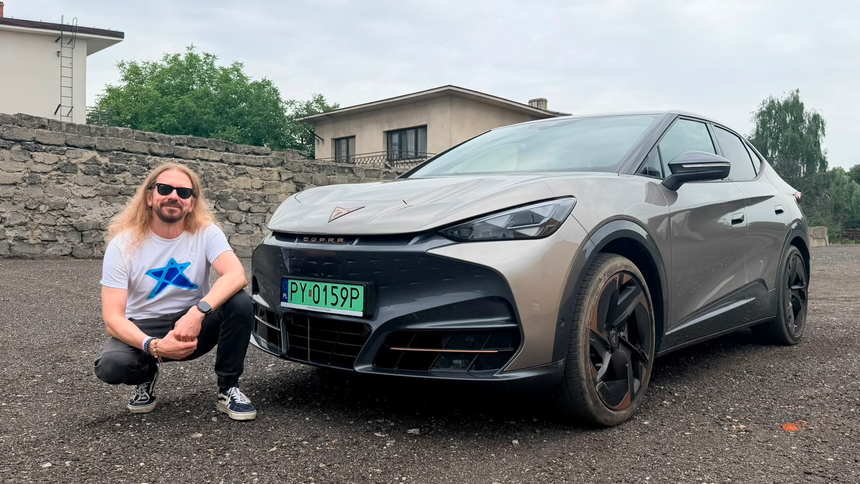 Mężczyzna z długimi włosami w okularach przeciwsłonecznych przy samochodzie marki CUPRA.