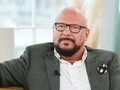 Mężczyzna w okularach, w szarym garniturze, siedzi na kanapie, wygląda na zamyślonego.