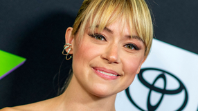 Tatiana Maslany. Uśmiechnięta osoba z jasnymi włosami i delikatnym makijażem, na tle ciemnych kolorów.
