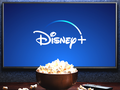Ekran telewizora z logo Disney+ oraz miską popcornu na stole.