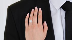 Na zdjęciu ręka z eleganckim pierścionkiem na tle czarnego garnituru.