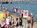 Widok plaży pełnej ludzi, znak zakazu kąpieli na pierwszym planie. Słońce, woda i wypoczywający.