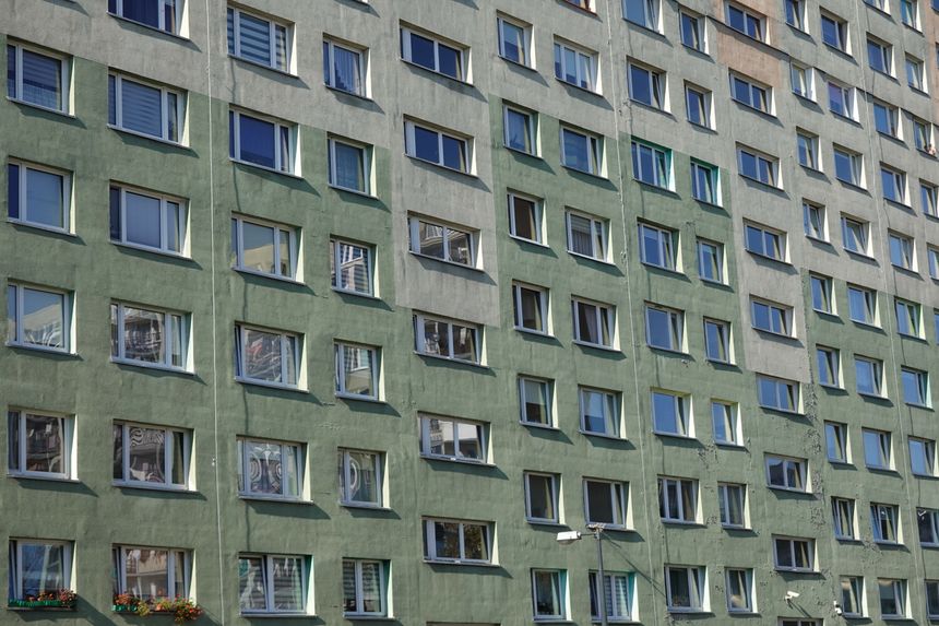Opis ALT: Fragment elewacji budynku mieszkalnego z zielonym tynkiem i oknami.