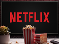 Na zdjęciu widoczna jest logo Netflixa na tle, obok popcorn i roślina doniczkowa.