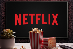 Na zdjęciu widoczna jest logo Netflixa na tle, obok popcorn i roślina doniczkowa.