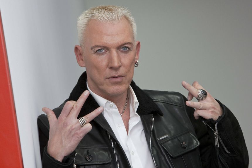 H.P. Baxxter w skórzanej kurtce z blond włosami, pokazujący dwa palce w geście.
