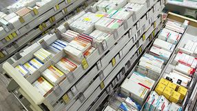Zgromadzenie leków w aptece, uporządkowane w plastikowych pojemnikach i szufladach.