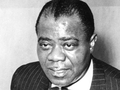 Louis Armstrong w garniturze, z wyrazem twarzy skupionym na rozmowie.