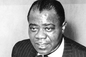 Louis Armstrong w garniturze, z wyrazem twarzy skupionym na rozmowie.