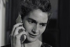 Kobieta mówi przez telefon, wygląda na zmartwioną, z krótkimi, falowanymi włosami.