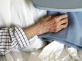 Zbliżenie na starą, zmarszczoną dłoń trzymającą niebieski koc na łóżku szpitalnym.