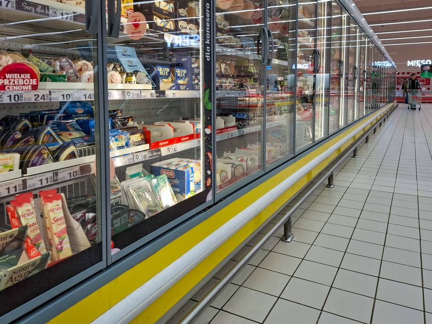 Widok półki z lodówkami w sklepie, pełnymi różnorodnych serów i produktów mlecznych.