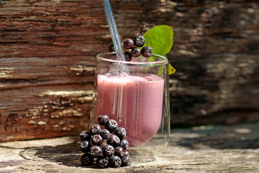 Szklanka różowego smoothie z owocami, ozdobiona jagodami i listkiem, na tle drewna.