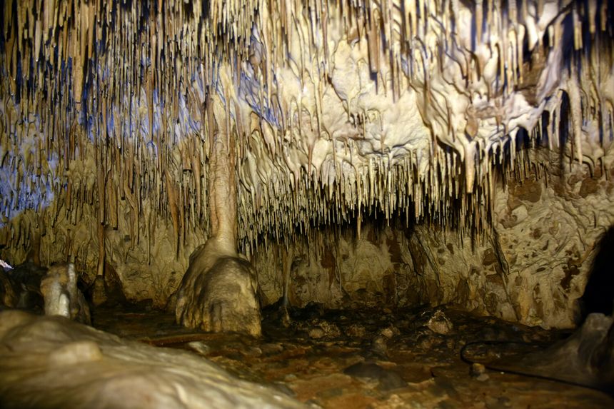 Wnętrze jaskini z stalaktytami i stalagmitami, oświetlone miękkim światłem.