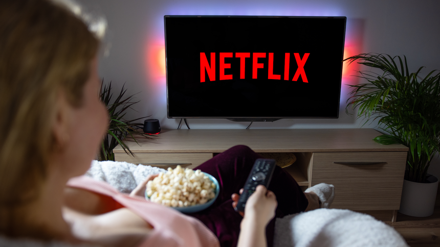 Kobieta siedzi na kanapie, trzymając miskę popcornu, patrzy na TV z napisem Netflix.