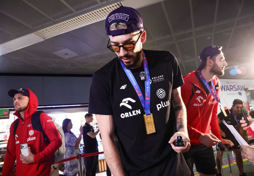 Tomasz Fornal w ciemnym T-shircie z medalem. W tle inni sportowcy i tłum ludzi na lotnisku.