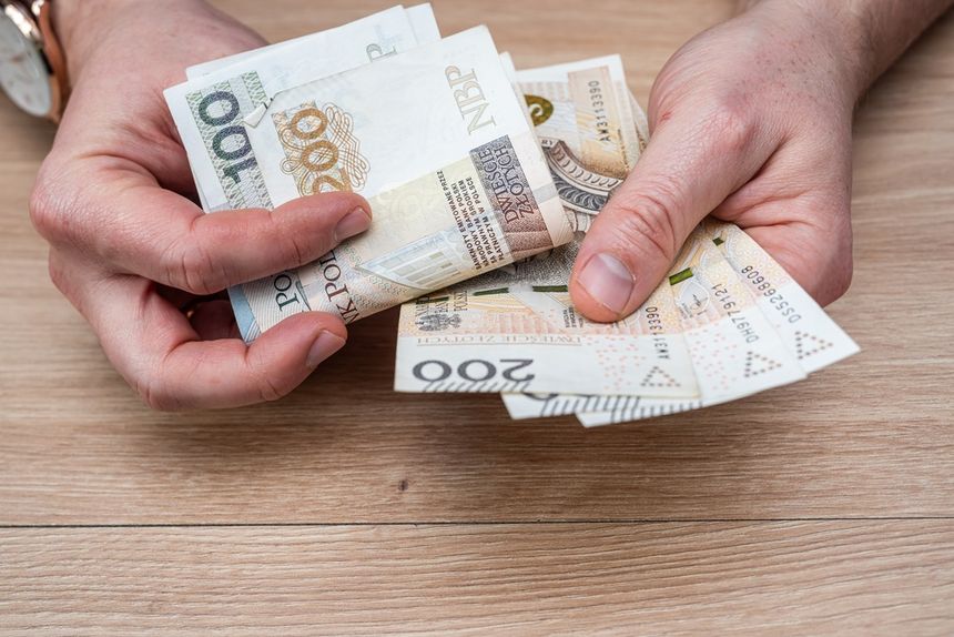 Zbliżenie na dłonie trzymające banknoty polskich złotych na drewnianym stole.