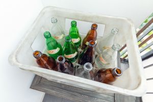 Kosz z pustymi butelkami w różnych kolorach: brązowe, zielone i przezroczyste.