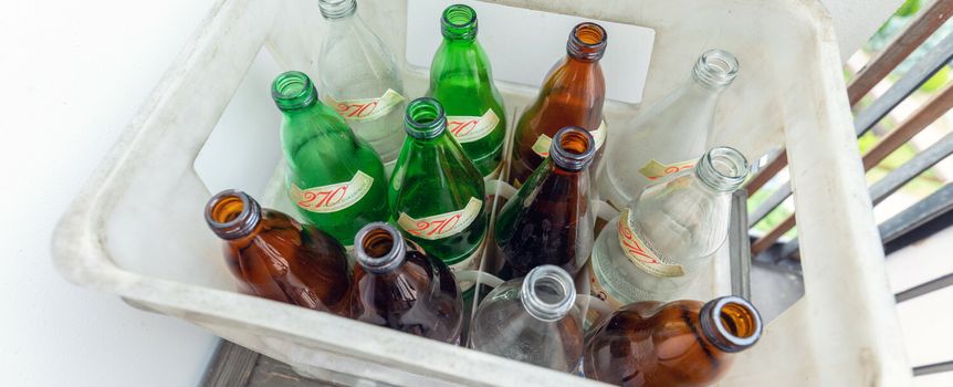 Kosz z pustymi butelkami w różnych kolorach: brązowe, zielone i przezroczyste.