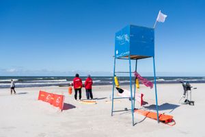 Na plaży z ratownikami w czerwonych strojach, wieżą ratunkową i morzem w tle.