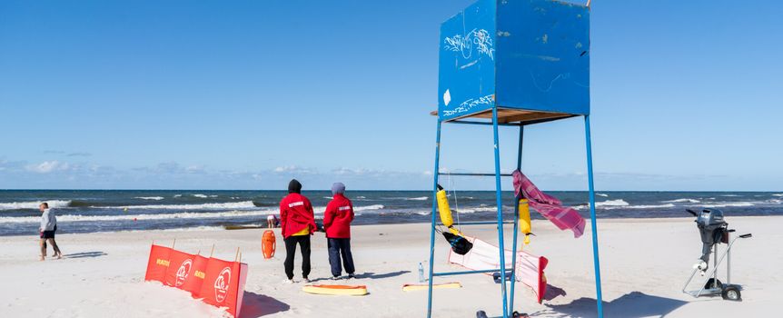 Na plaży z ratownikami w czerwonych strojach, wieżą ratunkową i morzem w tle.