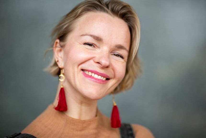 Kobieta z krótkimi blond włosami, uśmiechająca się, w czerwonych chwostach na uszach.