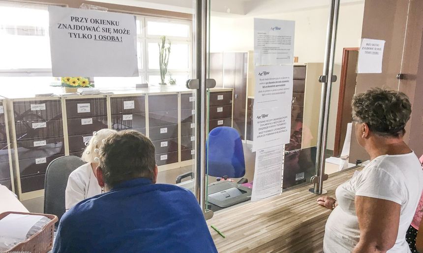 Na zdjęciu ludzie czekający przy oknie, z tablicą informującą o ograniczeniach.