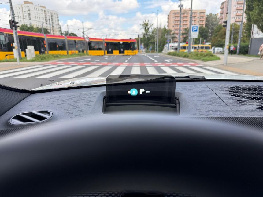 Widok z wnętrza samochodu na ulicę z tramwajem i przejściem dla pieszych. Słoneczne niebo.