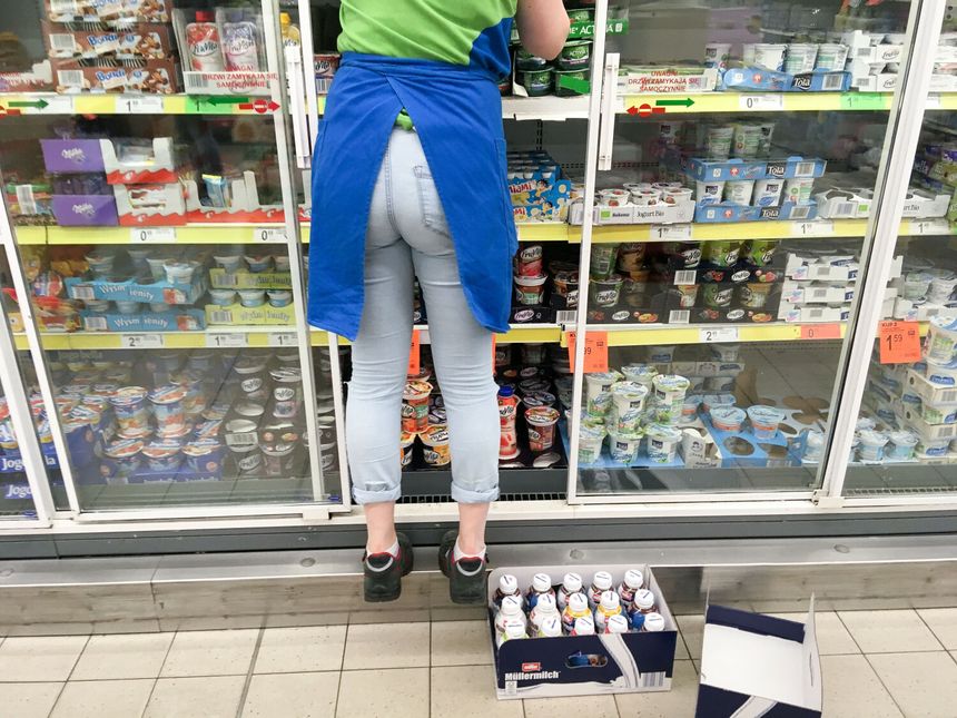 Pracownik sklepu stoi przed wystawą lodówek, sięgając po produkty z półki.