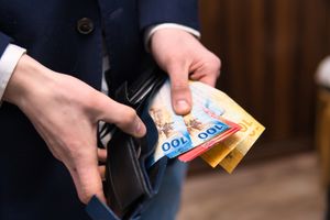 Mężczyzna trzyma skórzany portfel z banknotami o różnych nominałach.