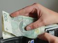 Osoba trzymająca banknot 100 zł otwiera portfel z innymi dokumentami.