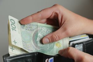 Osoba trzymająca banknot 100 zł otwiera portfel z innymi dokumentami.